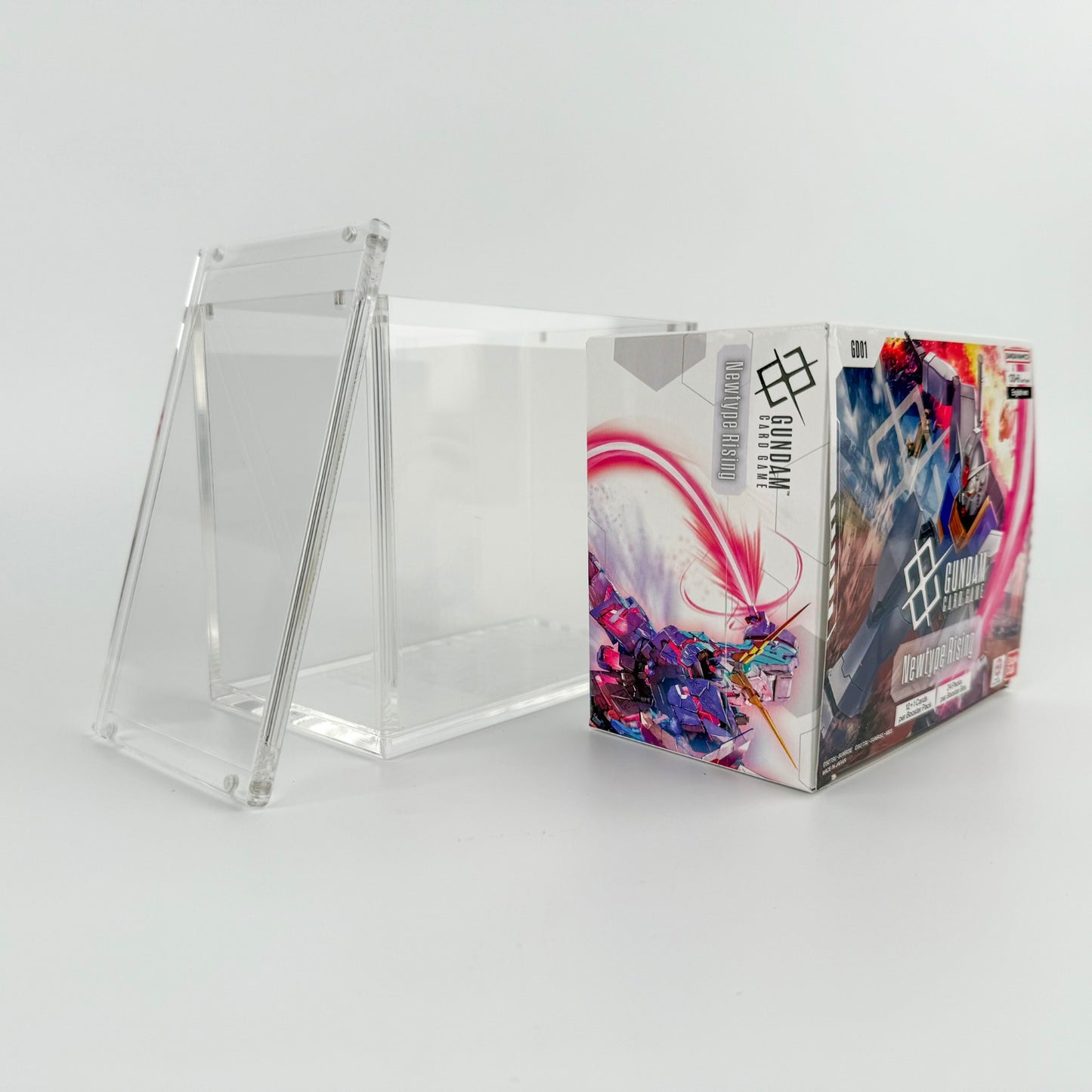 Clear acrylic display case with a magnetic lid, shown next to a Gundam TCG booster box.