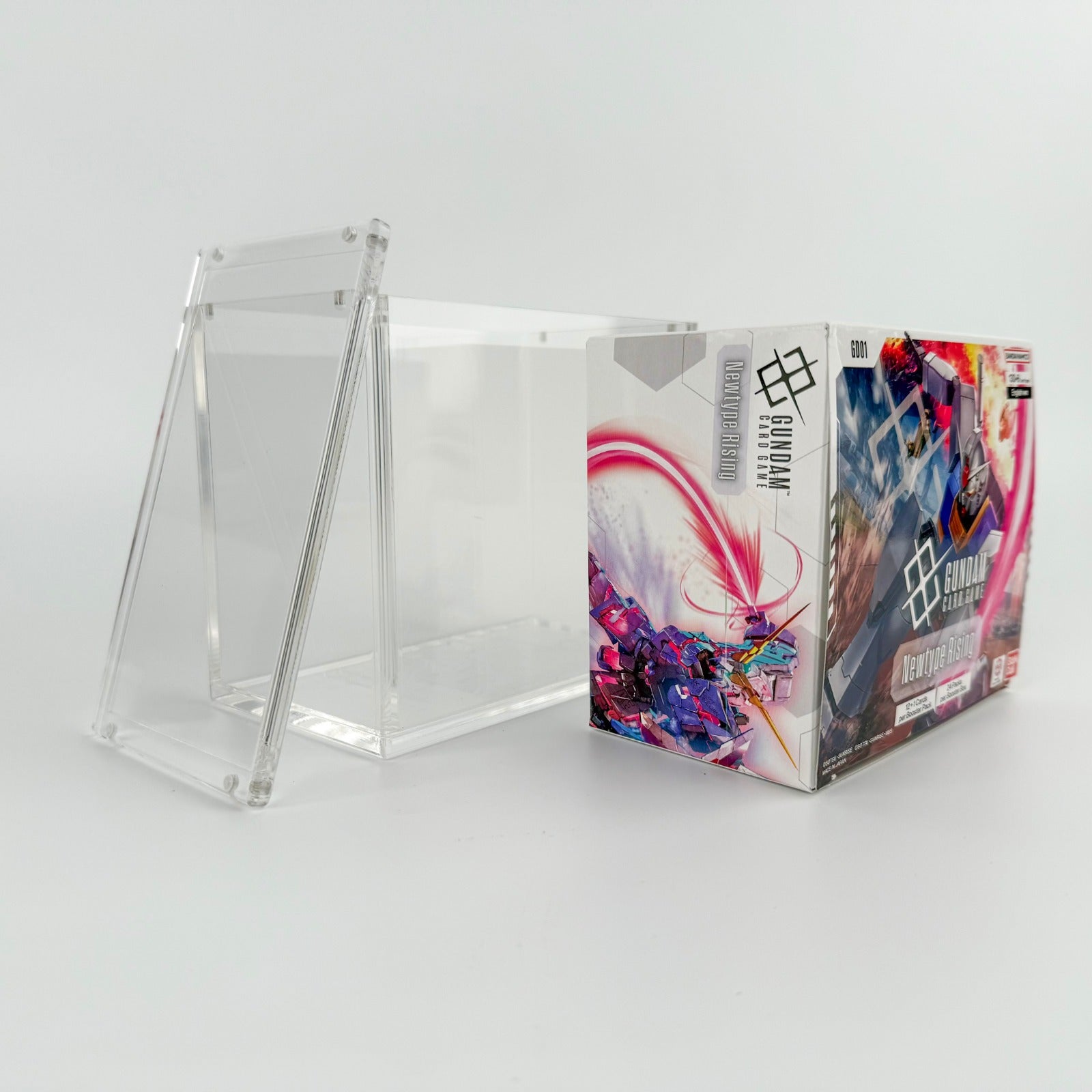 Clear acrylic display case with a magnetic lid, shown next to a Gundam TCG booster box.
