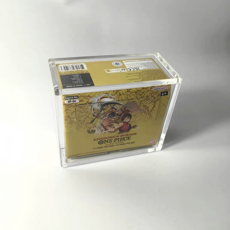 Clear acrylic display case protecting a gold One Piece TCG booster box, featuring a magnetic top closure.