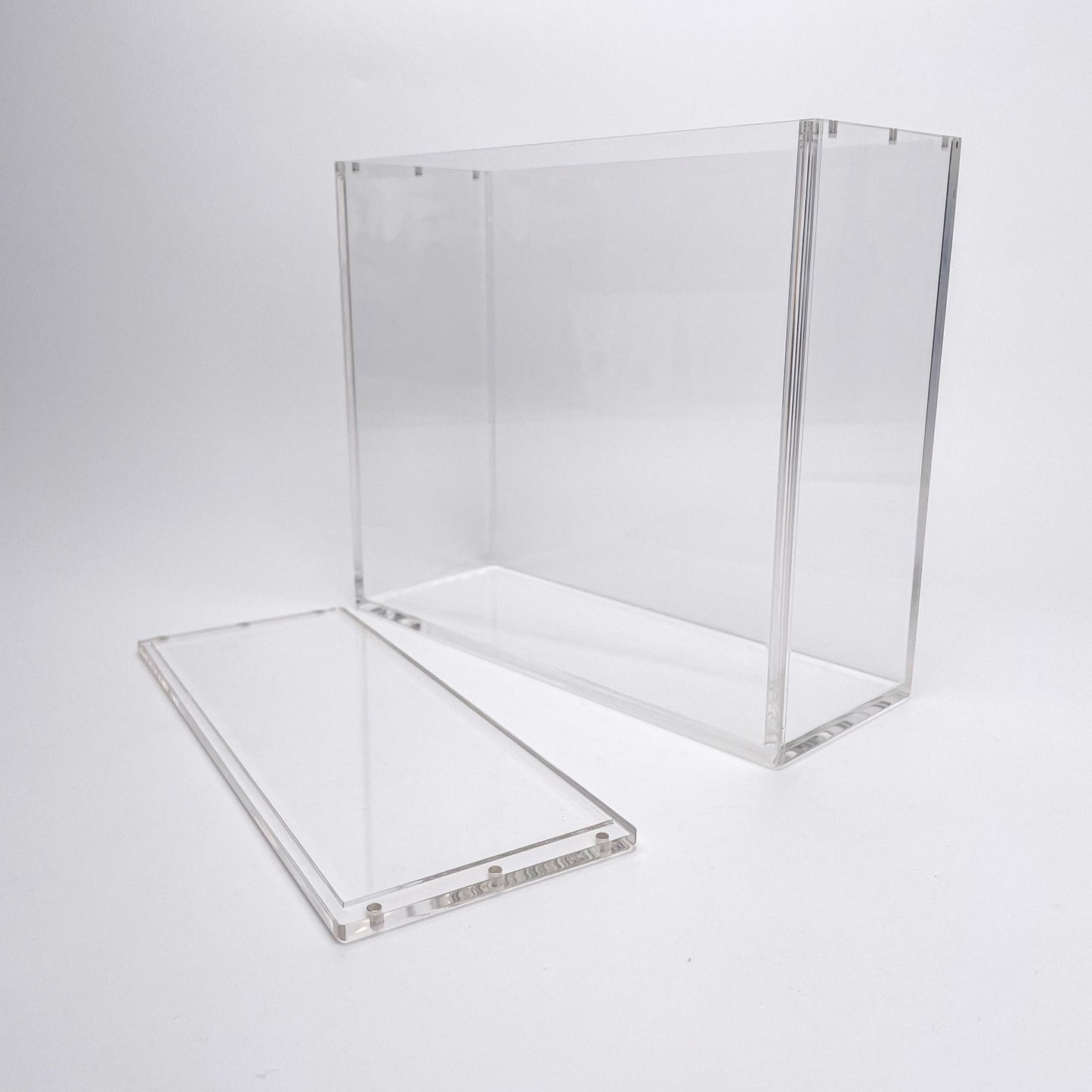 Clear acrylic display case for TCG booster boxes with a magnetic, removable top lid on a white background.