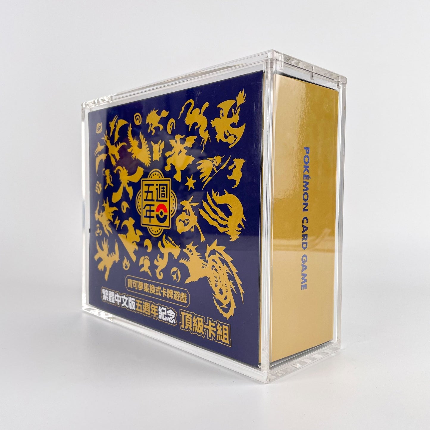 Clear acrylic display case protecting a blue and gold Chinese 5th Anniversary Pokémon TCG collection box.