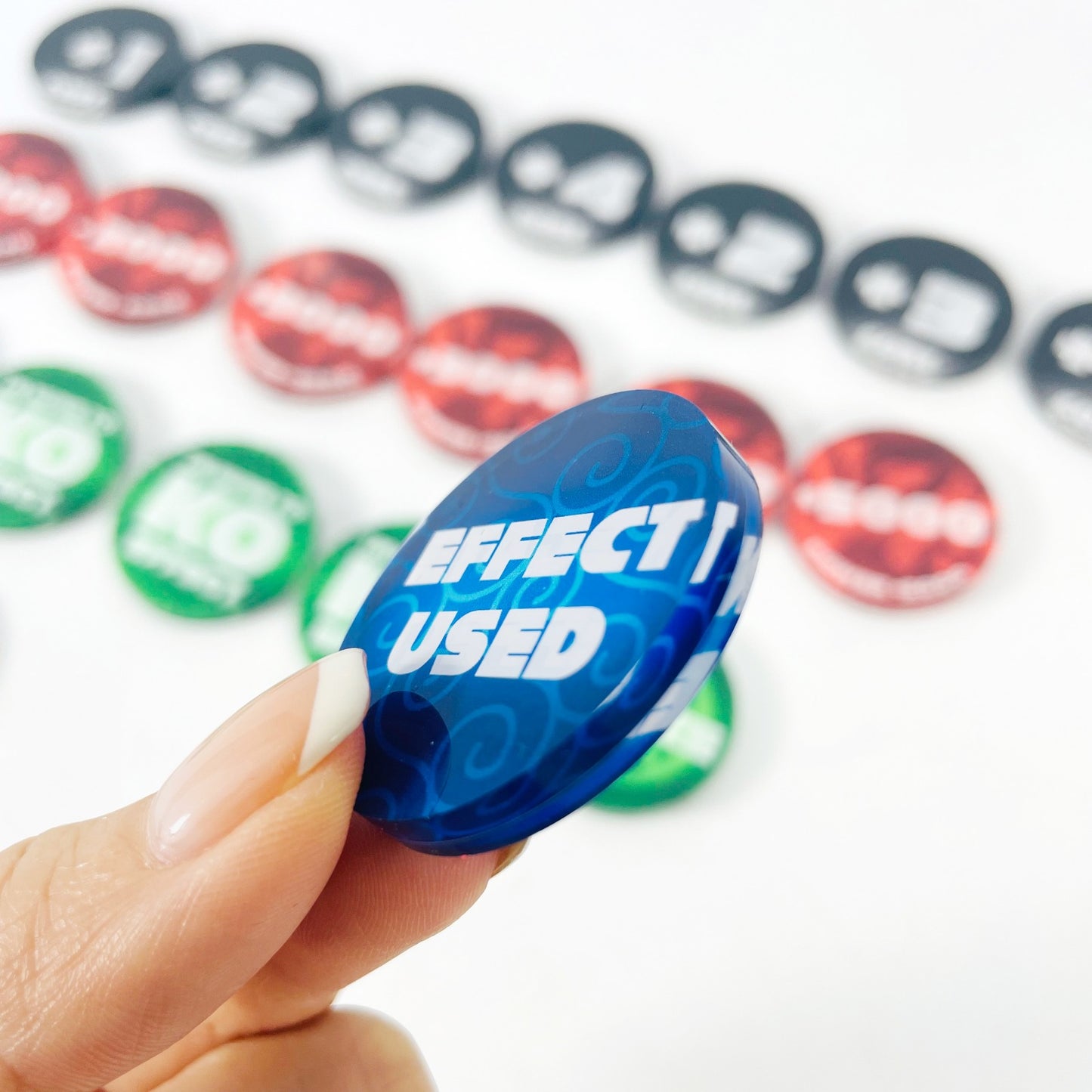 Hand holding a blue acrylic "Effect Used" token, with red, green, and black One Piece Card Game tokens blurred in the background.
