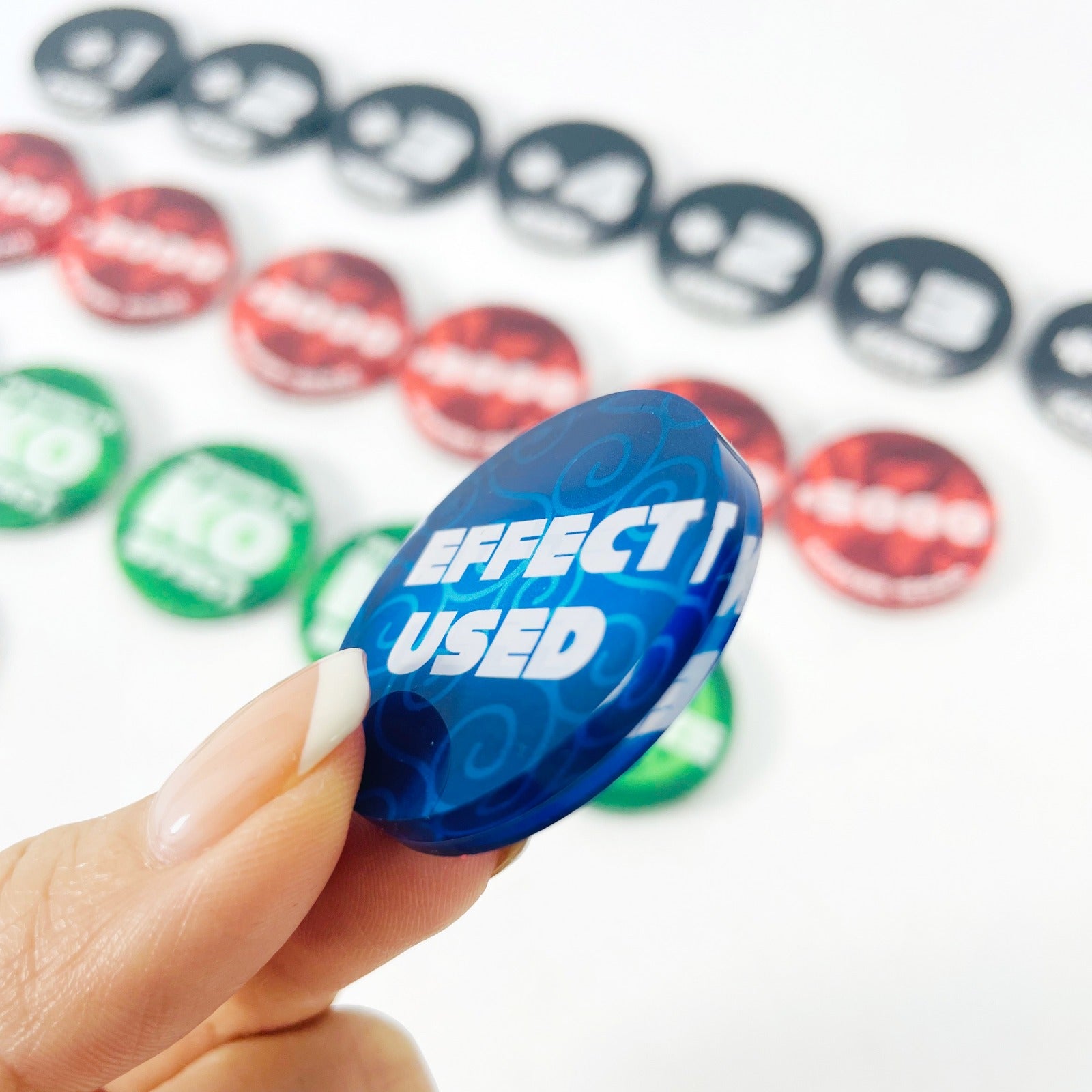 Hand holding a blue acrylic "Effect Used" token, with red, green, and black One Piece Card Game tokens blurred in the background.