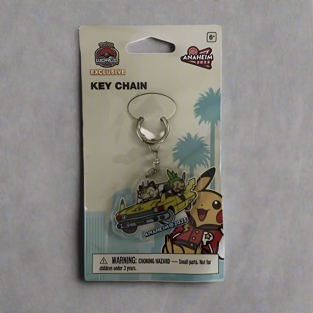 Pokémon 2025 WCS keychain featuring Meowth and Chespin in a yellow car, packaged on a branded Anaheim display card.