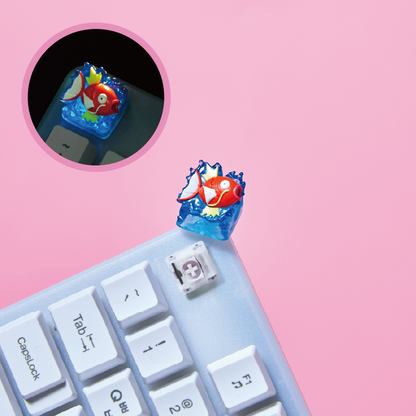 Magikarp resin keycap featuring a red fish in blue water, mounted on a white mechanical keyboard against a pink background.