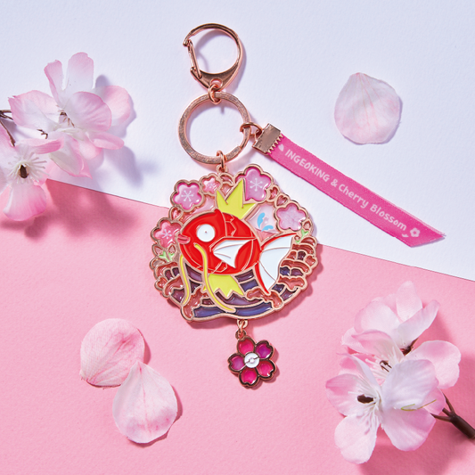 Magikarp keychain with liquid glitter, cherry blossom frame, and pink ribbon on a two-tone pink and white background.