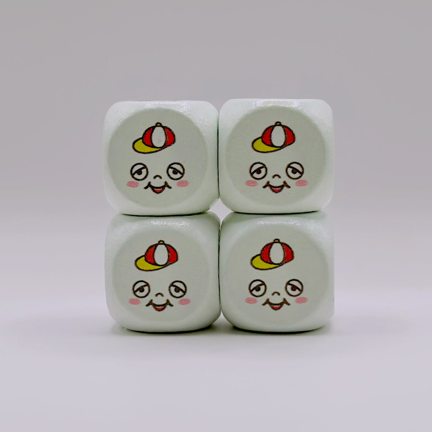 Four 16mm wooden dice with rounded corners, featuring a custom UV-ink cartoon face design on a light green background.